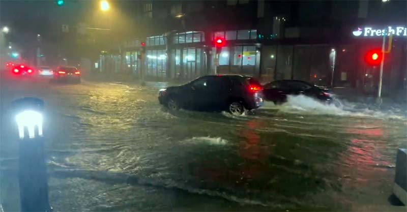Cars drive through flooded streets at night