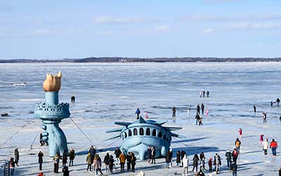 People walking on frozen Lake Mendota, getting an up-close view of Lady Liberty appearing to emerge through the ice