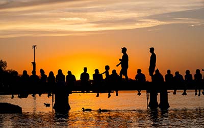 A group of college students sitting on a pier silhouetted against a sunset